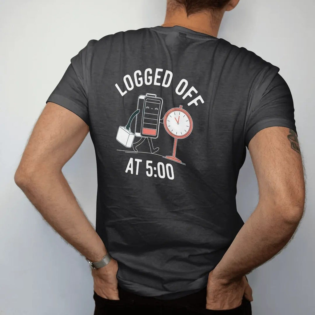 Man wearing a Black tee, seen from the back: minimal single-line drawing of a sleepy battery walking away from a punch clock carrying a lunchbox, with "LOGGED OFF / AT 5:00" in small spaced-out caps, printed in bone white with a low-battery red…