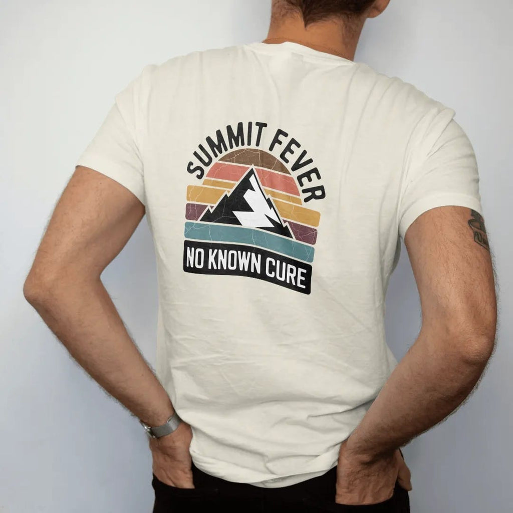 Man wearing a Ivory tee, seen from the back: a vintage medicine-label badge with a mountain peak and a thermometer reading off the chart, faded 70s souvenir style, lettered "SUMMIT FEVER / NO KNOWN CURE" in chunky rounded 70s serif letters with a…