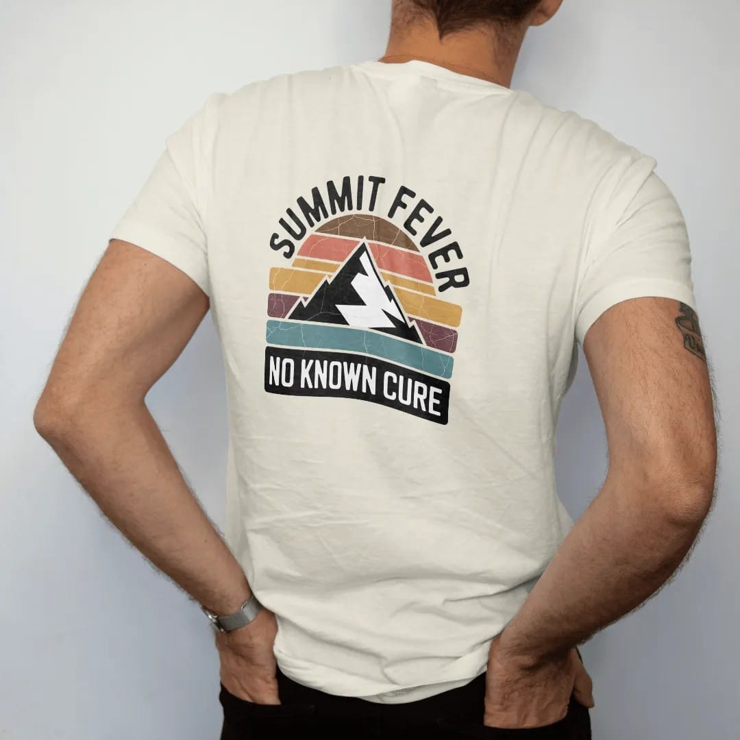 Man wearing a Ivory tee, seen from the back: a vintage medicine-label badge with a mountain peak and a thermometer reading off the chart, faded 70s souvenir style, lettered "SUMMIT FEVER / NO KNOWN CURE" in chunky rounded 70s serif letters with a…