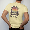 Man wearing a Butter tee, seen from the back: a hammock strung between two pines with boots kicked off and a cold drink below, faded 70s souvenir style, lettered "ZERO DAY / ENTHUSIAST" in chunky rounded 70s letters with a drop shadow, printed in…