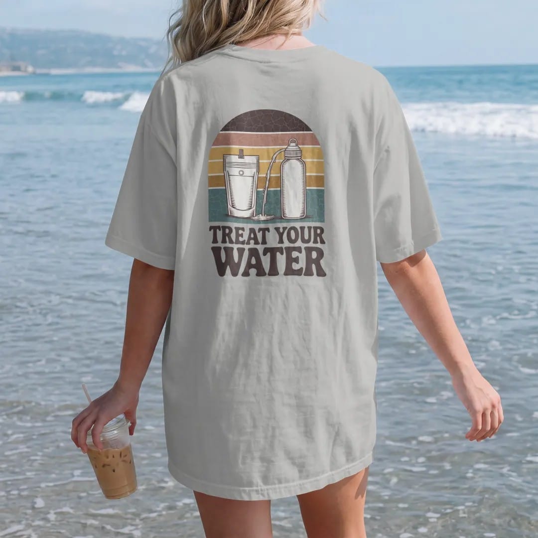 Woman on the beach in a Granite tee, back view: a mountain stream flowing into a squeeze filter pouch and a water bottle, field-guide layout, faded 70s souvenir style, lettered "TREAT YOUR WATER" in chunky rounded 70s serif letters with a drop…