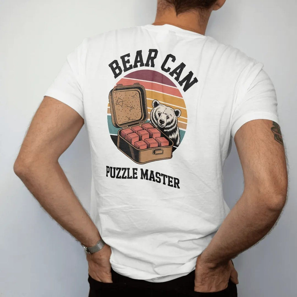 Man wearing a White tee, seen from the back: an open bear canister with food items stacked in tidy blocks and a bear peeking from behind a rock, faded 70s souvenir style, lettered "BEAR CAN / PUZZLE MASTER" in chunky rounded 70s letters with a drop…