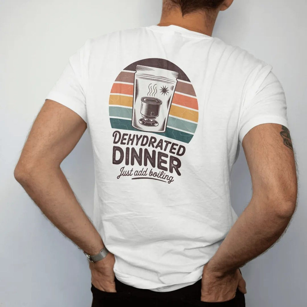 Man wearing a White tee, seen from the back: a retro food-pouch package with a steaming camp stove and a starburst callout, faded 70s souvenir style, lettered "DEHYDRATED DINNER / JUST ADD BOILING" in chunky rounded 70s letters with a drop shadow…