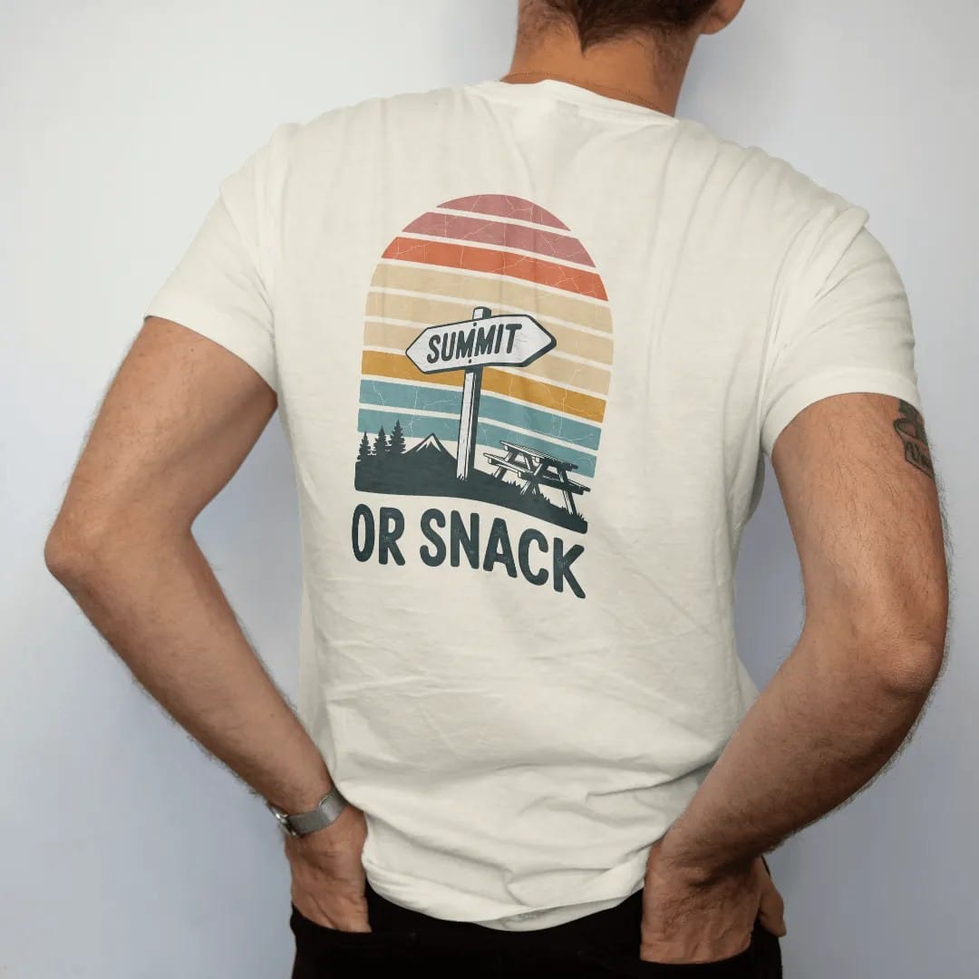 Man wearing a Ivory tee, seen from the back: a trail junction sign with one arrow pointing to a peak and one to a picnic table, faded 70s souvenir style, lettered "SUMMIT / OR SNACK" in chunky rounded 70s letters with a drop shadow, printed in…