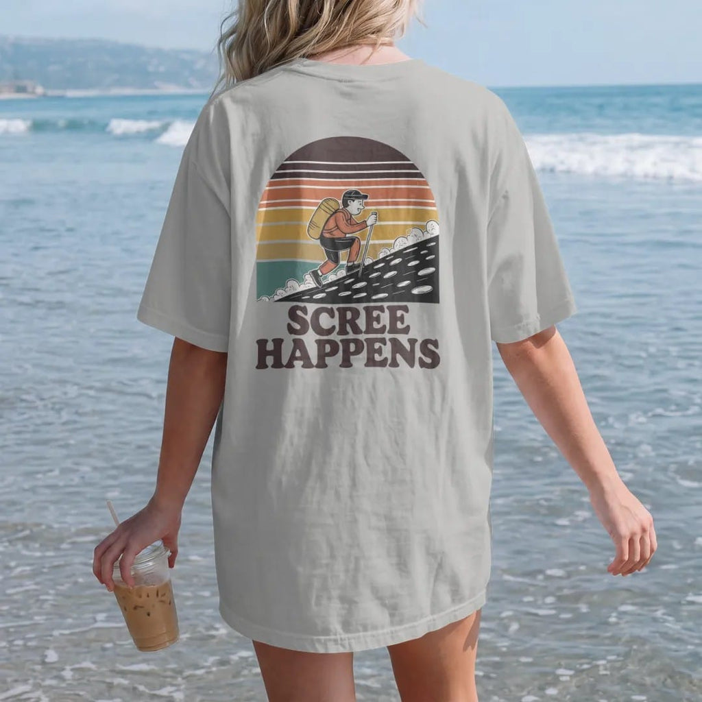 Woman on the beach in a Granite tee, back view: a cartoon hiker sliding down a slope of loose rocks with little dust clouds, faded 70s souvenir style, lettered "SCREE HAPPENS" in chunky rounded 70s letters with a drop shadow, printed in faded…