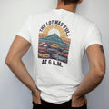 Man wearing a White tee, seen from the back: a packed trailhead parking lot with tiny cars and a mountain behind, a sad sun rising, faded 70s souvenir style, lettered "THE LOT WAS FULL / AT 6 A.M." in chunky rounded 70s letters with a drop shadow,…