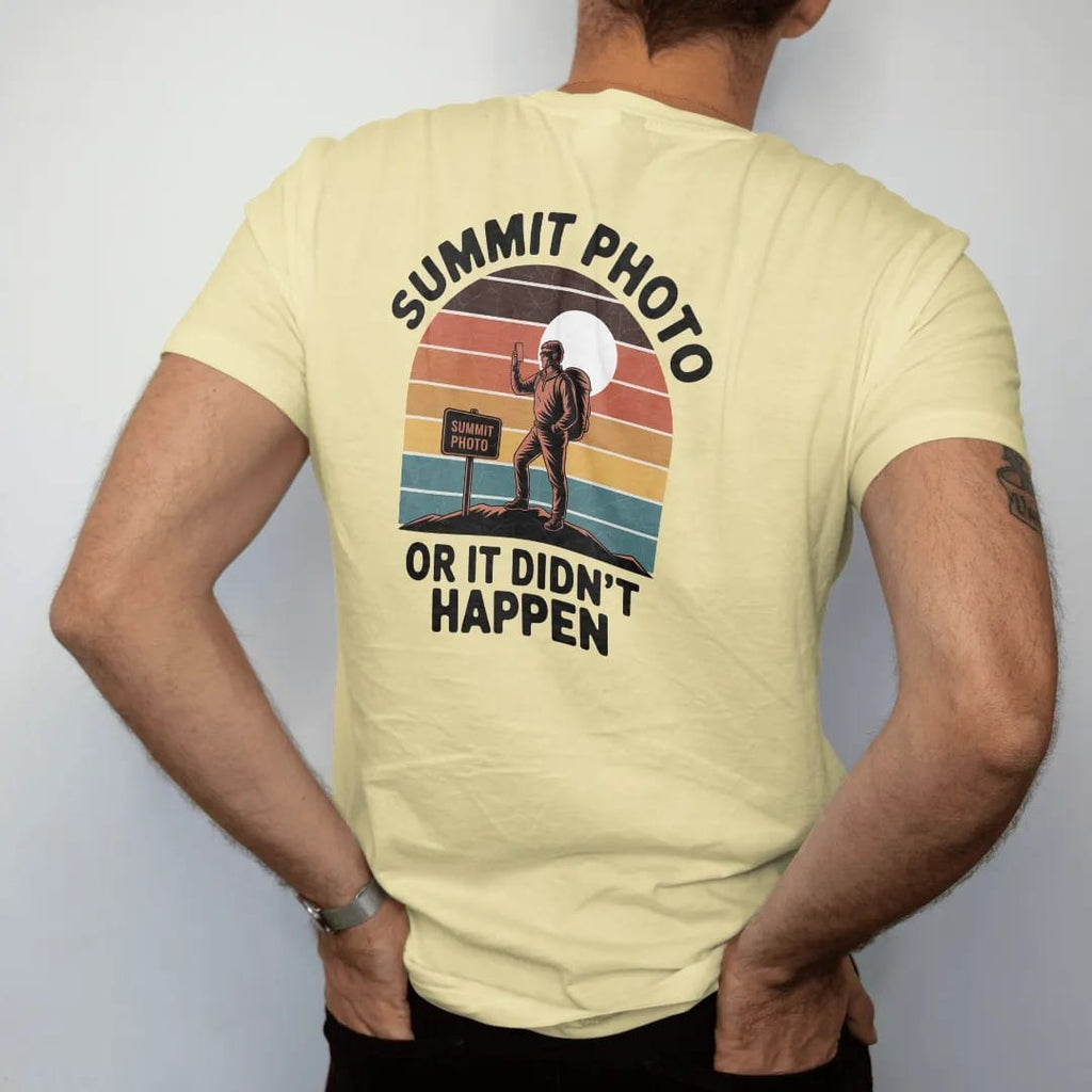 Man wearing a Butter tee, seen from the back: a hiker posing with a phone beside a summit sign under a bright sun, faded 70s souvenir style, lettered "SUMMIT PHOTO / OR IT DIDN'T HAPPEN" in chunky rounded 70s letters with a drop shadow, printed in…