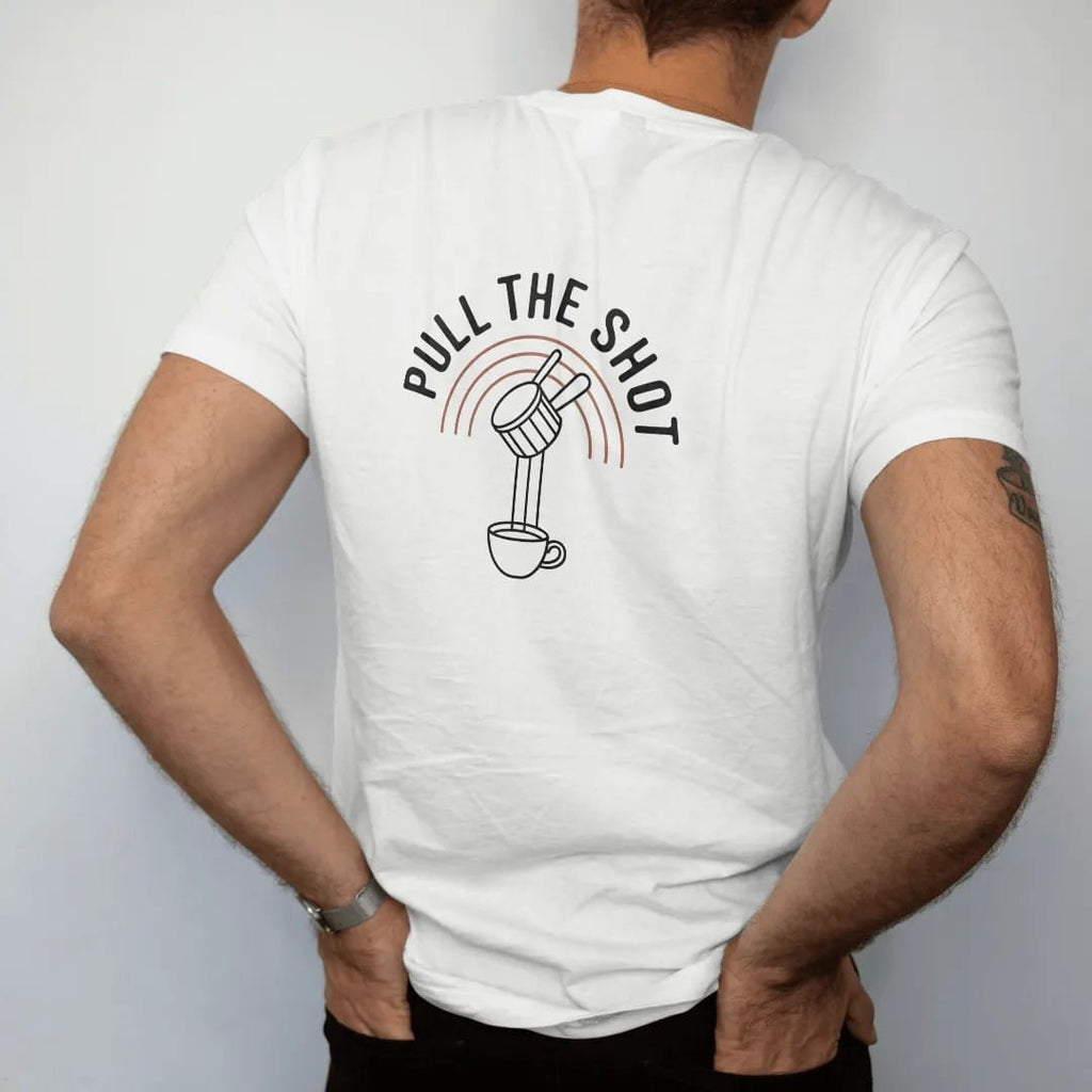 Man wearing a White tee, seen from the back: a portafilter dripping two streams of espresso into a cup over thin arc lines with Pull The Shot stacked on top, drawn in a single fine crema-cream line with one burnt copper accent.