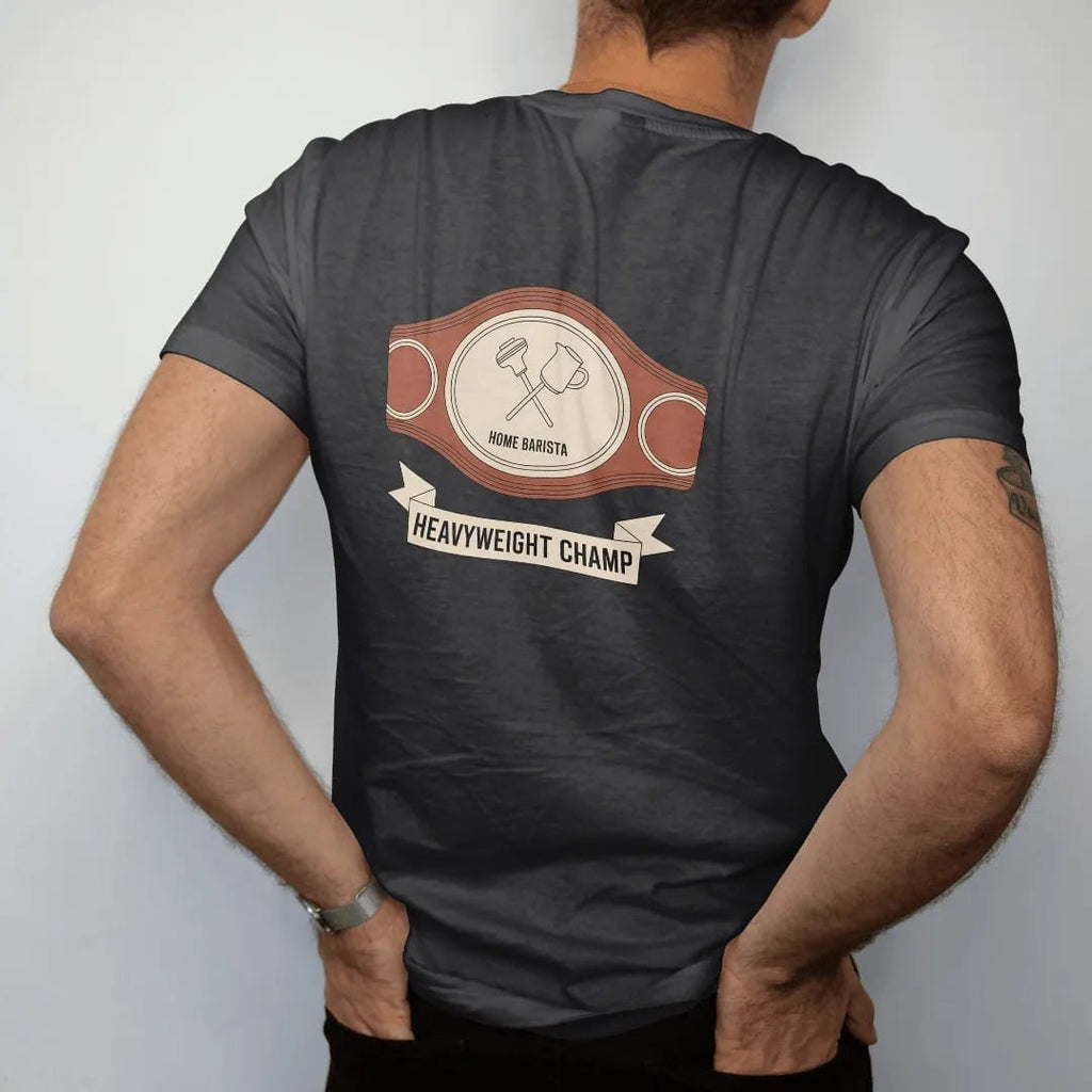 Man wearing a Black tee, seen from the back: a championship belt with a crossed tamper and milk pitcher on the plate, Home Barista across it and Heavyweight Champ on a ribbon, drawn in a single fine crema-cream line with one burnt copper accent.