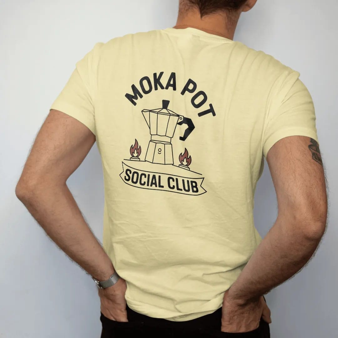 Man wearing a Butter tee, seen from the back: a sputtering stovetop moka pot over a small gas flame with Moka Pot curved above and Social Club in a banner, drawn in a single fine roast-brown line with one burnt copper accent.