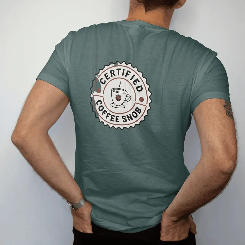Man wearing a Blue Spruce tee, seen from the back: a scalloped official seal with a monocled coffee cup, Certified across the top and Coffee Snob on a ribbon, drawn in a single fine roast-brown line with one burnt copper accent.
