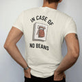 Man wearing a Ivory tee, seen from the back: an emergency break-glass box holding a bag of coffee beans with a little hammer, In Case Of above and No Beans below, drawn in a single fine crema-cream line with one burnt copper accent.