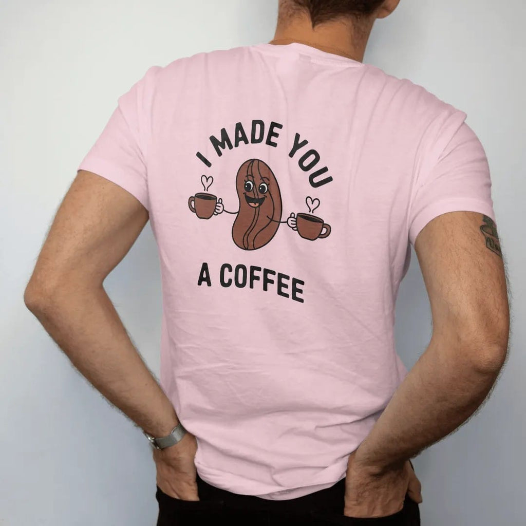 Man wearing a Blossom tee, seen from the back: a smiling coffee-bean mascot offering two steaming mugs with a heart in the steam, under I Made You and over A Coffee, drawn in a single fine roast-brown line with one burnt copper accent.