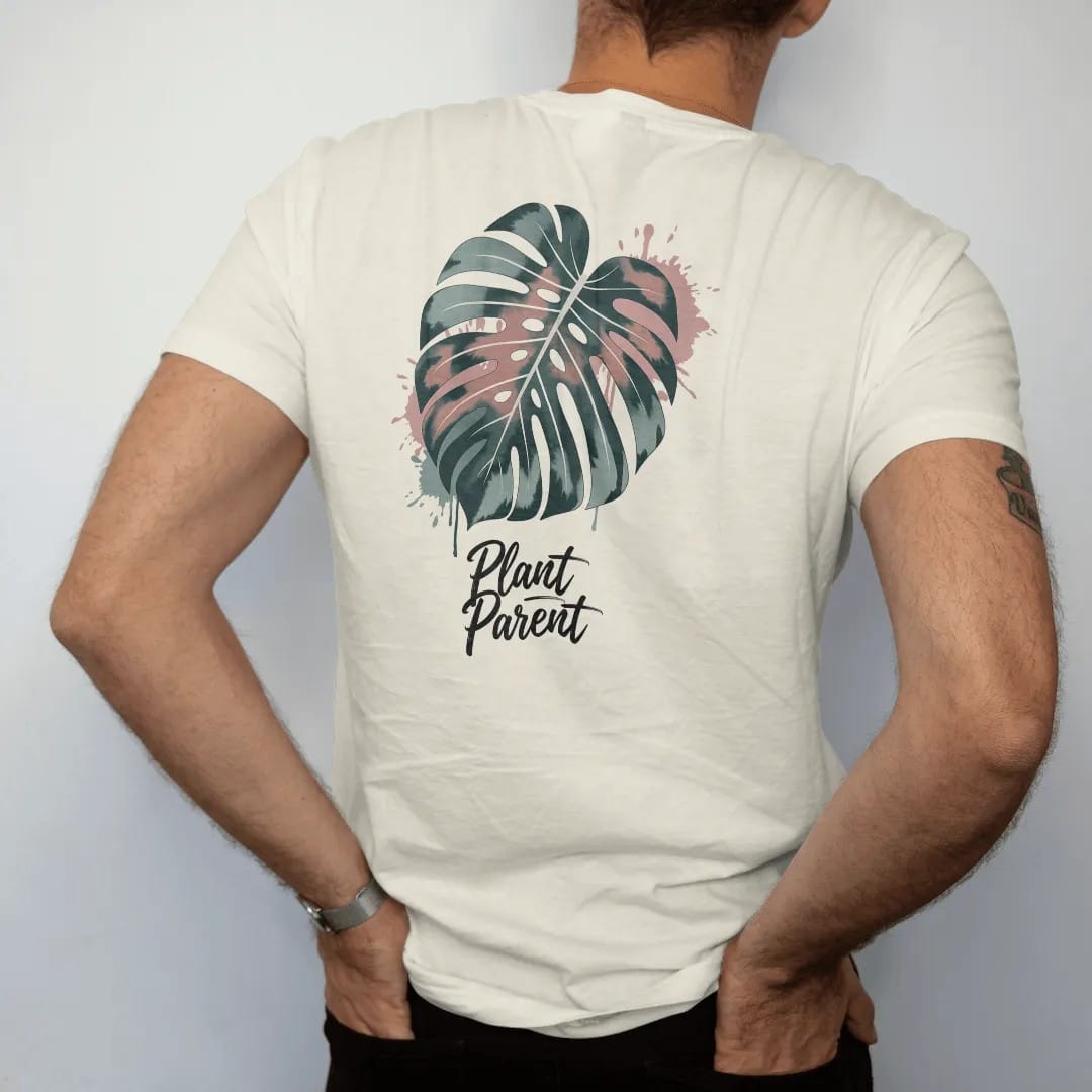 Man wearing a Ivory tee, seen from the back: a single large monstera leaf with split fenestrations, small brush-written caps "PLANT PARENT" beneath, painted in loose watercolor and ink with soft deep green, terracotta, soil brown and moss washes.