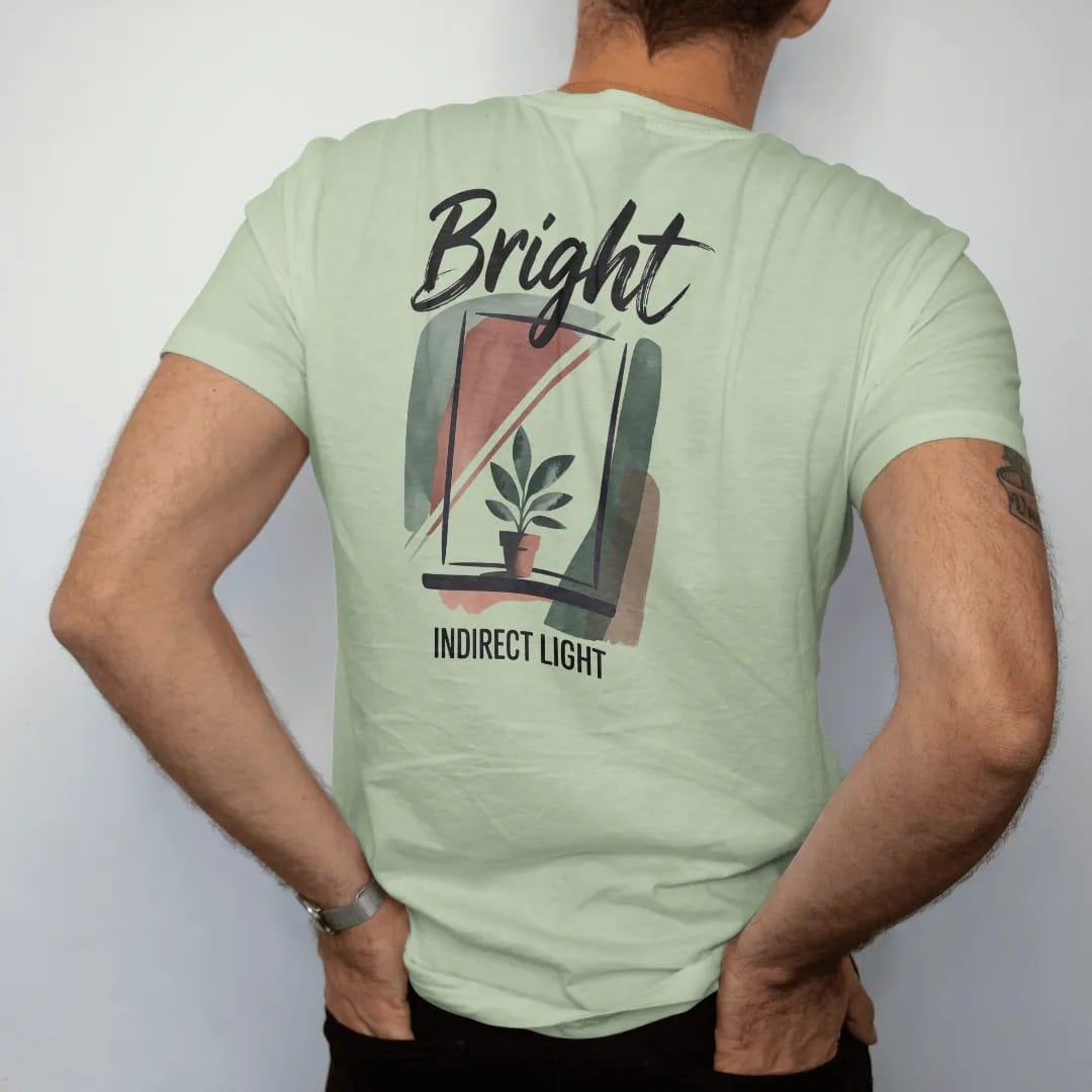 Man wearing a Light Green tee, seen from the back: a simple window with soft angled light rays falling on a small potted plant, "BRIGHT" in loose brush script above and "INDIRECT LIGHT" small below, painted in loose watercolor and ink with soft…