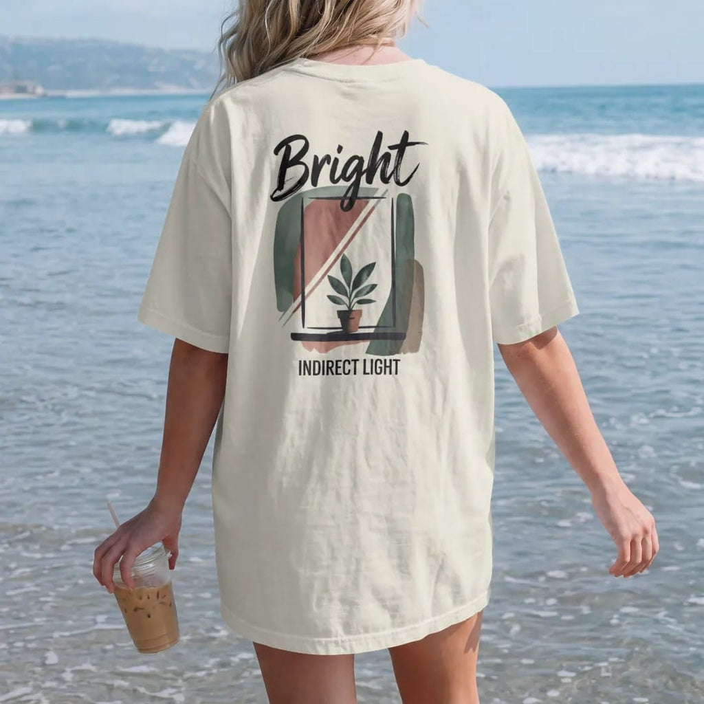 Woman on the beach in a Ivory tee, back view: a simple window with soft angled light rays falling on a small potted plant, "BRIGHT" in loose brush script above and "INDIRECT LIGHT" small below, painted in loose watercolor and ink with soft deep…