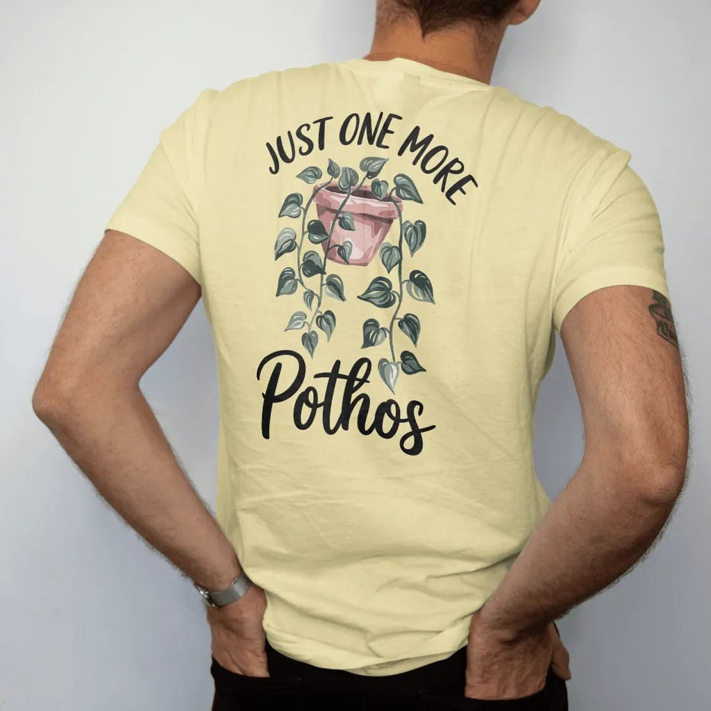 Man wearing a Butter tee, seen from the back: a trailing pothos vine draping from a small hanging pot with heart-shaped leaves, "JUST ONE MORE" in small brush-written caps above and "POTHOS" in loose brush script below, painted in loose watercolor…
