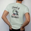 Man wearing a Bay tee, seen from the back: a small droopy plant beside a tipped-over watering can with a puddle, "I LOVED IT" in loose brush script above and "TOO MUCH" in small brush-written caps below, painted in loose watercolor and ink with…