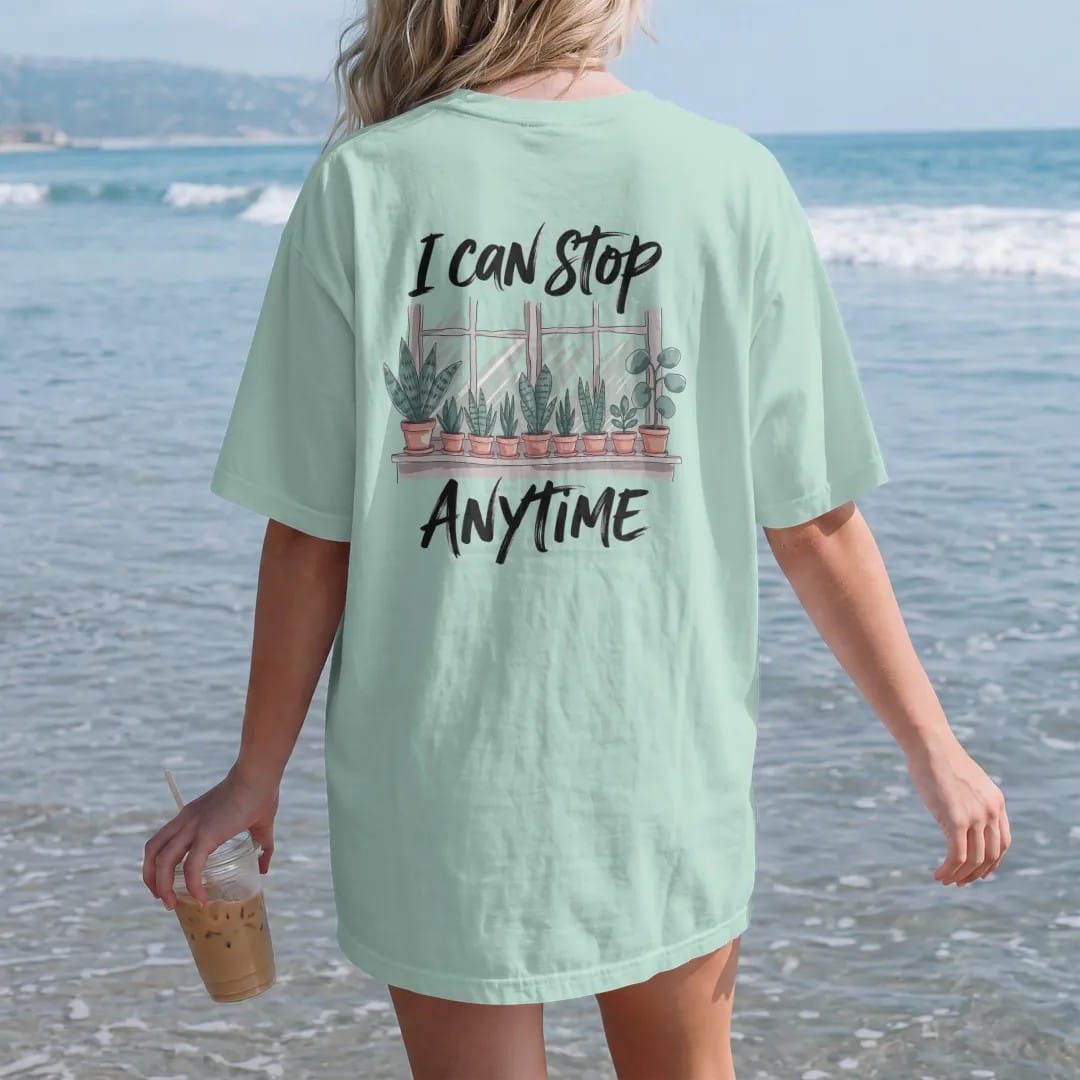 Woman on the beach in a Chalky Mint tee, back view: a crowded windowsill of nine small potted plants, each a different leaf shape, "I CAN STOP" in loose brush script above and "ANYTIME" in small brush-written caps below, painted in loose watercolor…