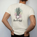 Man wearing a Ivory tee, seen from the back: a tall snake plant with upright striped leaves in a simple pot, loose brush script "HARD TO KILL" beneath, painted in loose watercolor and ink with soft mint, clay pink, cream and lime washes.