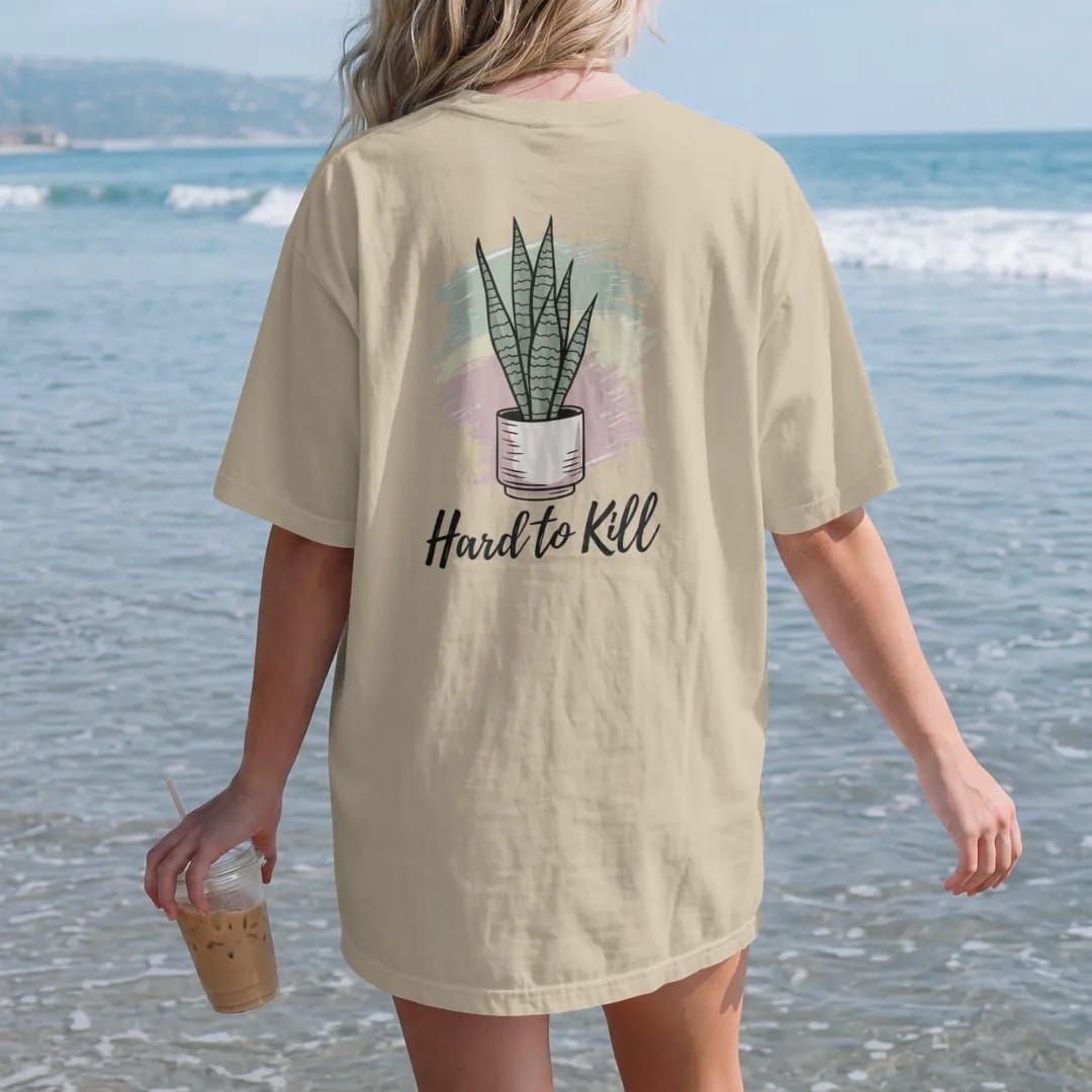 Woman on the beach in a Sandstone tee, back view: a tall snake plant with upright striped leaves in a simple pot, loose brush script "HARD TO KILL" beneath, painted in loose watercolor and ink with soft mint, clay pink, cream and lime washes.
