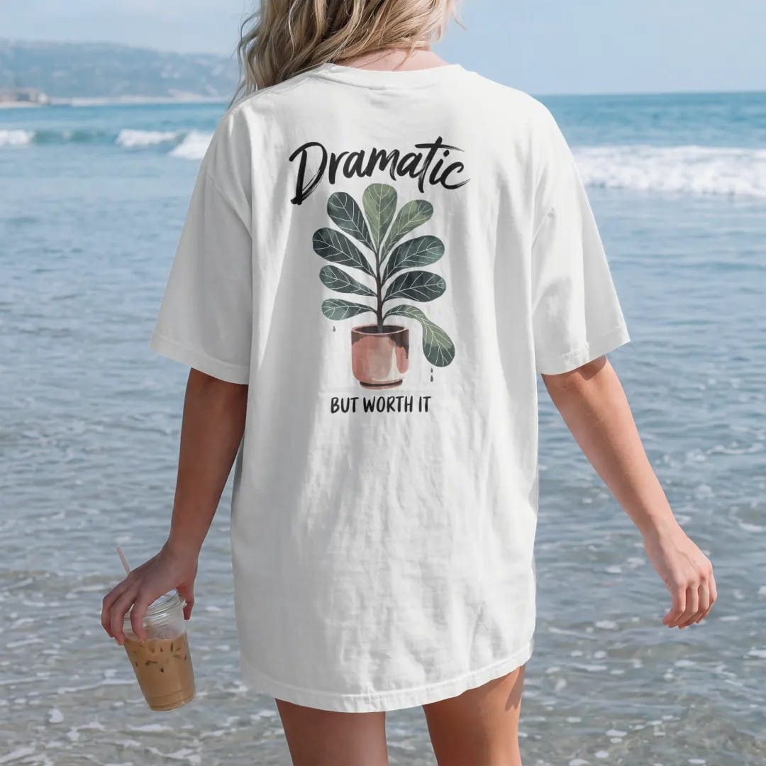 Woman on the beach in a White tee, back view: a fiddle leaf fig in a tall pot with one leaf dropping dramatically, "DRAMATIC" in loose brush script above and "BUT WORTH IT" small below, painted in loose watercolor and ink with soft deep green,…
