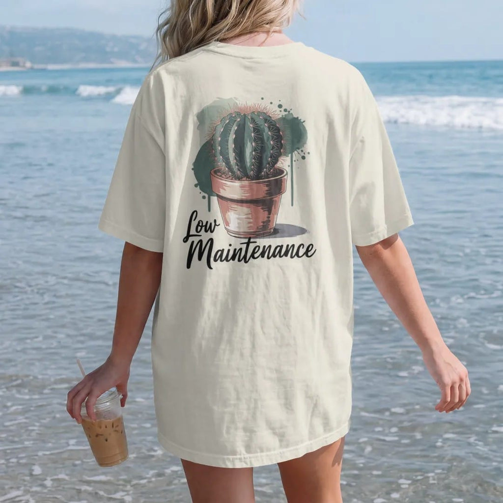 Woman on the beach in a Ivory tee, back view: a single round cactus in a small terracotta pot, small brush-written caps "LOW MAINTENANCE" beneath, painted in loose watercolor and ink with soft deep green, terracotta, soil brown and moss washes.