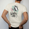 Man wearing a Ivory tee, seen from the back: a vintage watering can tilted mid-pour with three clean drops, "WATER ME" in hand-lettered brush script beneath, painted in loose watercolor and ink with soft mint, clay pink, cream and lime washes.