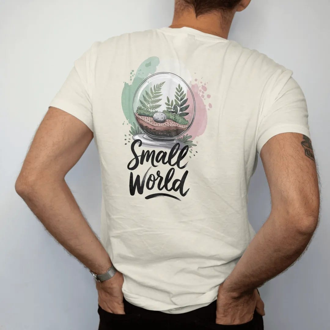 Man wearing a Ivory tee, seen from the back: a glass globe terrarium with tiny ferns, moss and a pebble inside, "SMALL WORLD" in loose brush script beneath, painted in loose watercolor and ink with soft mint, clay pink, cream and lime washes.