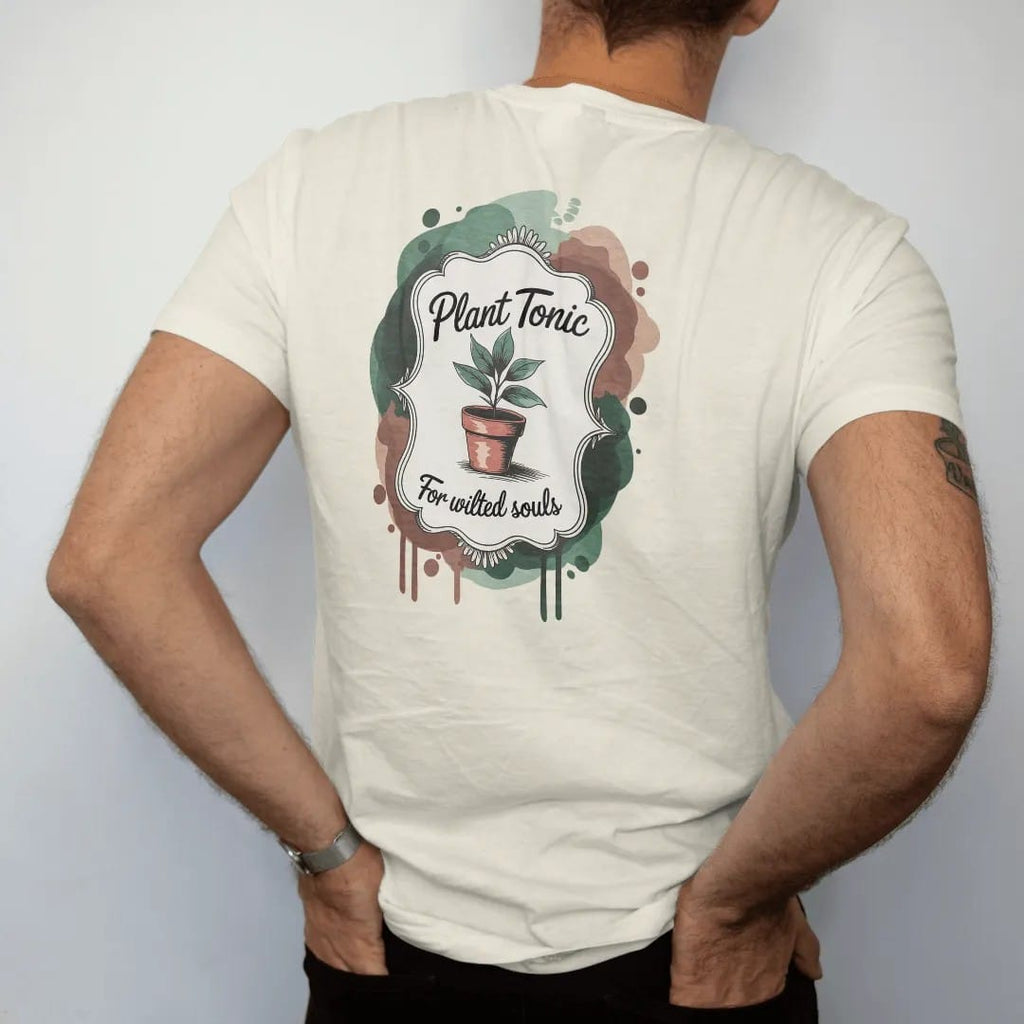 Man wearing a Ivory tee, seen from the back: vintage seed-packet ad parody with a small potted plant inside an ornate label frame, "PLANT TONIC" in loose brush script and "FOR WILTED SOULS" in hand-lettered brush script below, painted in loose…