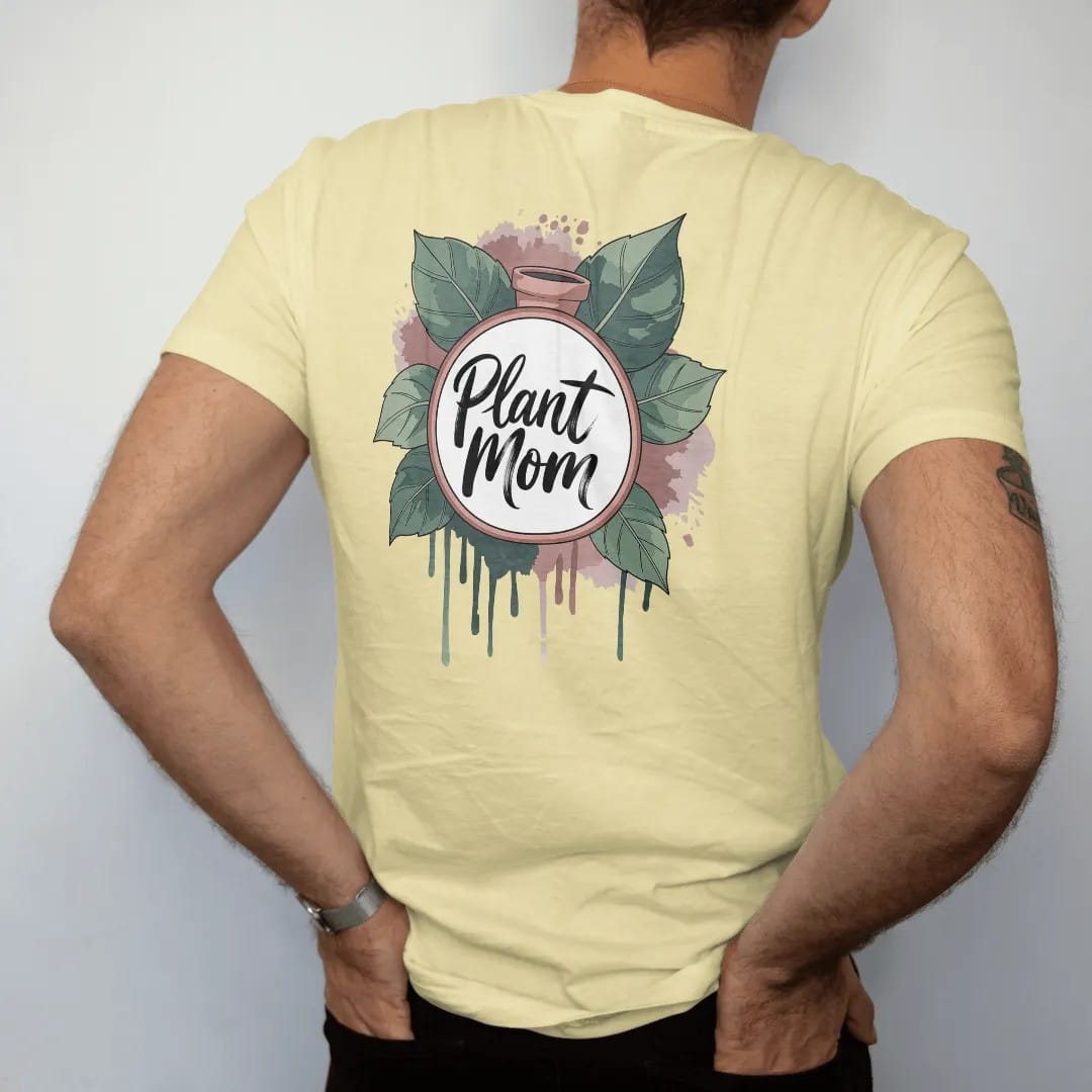 Man wearing a Butter tee, seen from the back: a neat round badge framed by two pothos leaves with a small pot in the center, "PLANT MOM" in loose brush script across the bottom, painted in loose watercolor and ink with soft deep green, terracotta,…