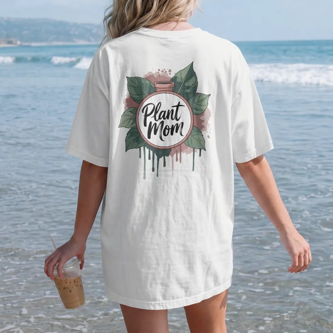 Woman on the beach in a White tee, back view: a neat round badge framed by two pothos leaves with a small pot in the center, "PLANT MOM" in loose brush script across the bottom, painted in loose watercolor and ink with soft deep green, terracotta,…