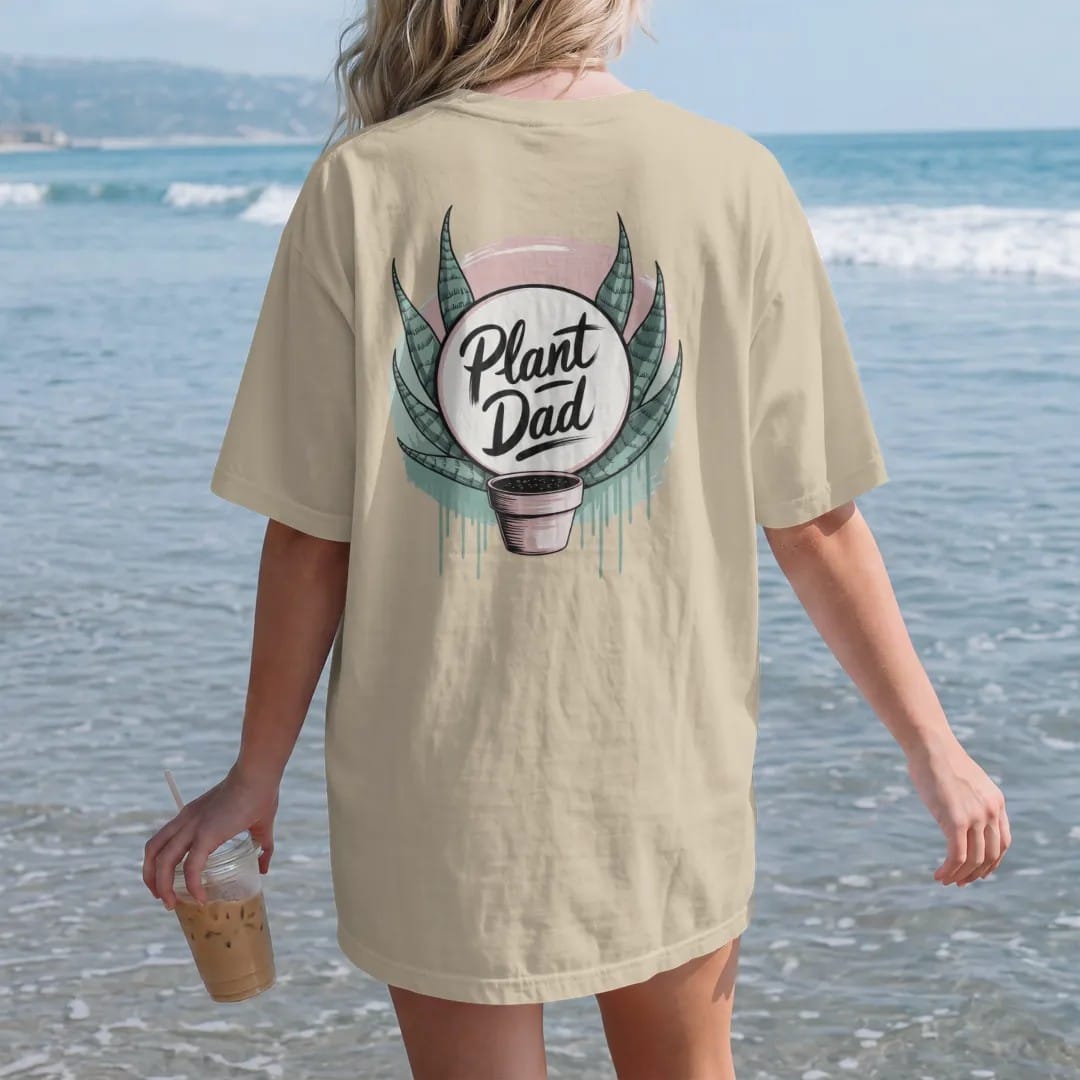 Woman on the beach in a Sandstone tee, back view: a neat round badge framed by two snake-plant leaves with a small pot in the center, "PLANT DAD" in loose brush script across the bottom, painted in loose watercolor and ink with soft mint, clay…