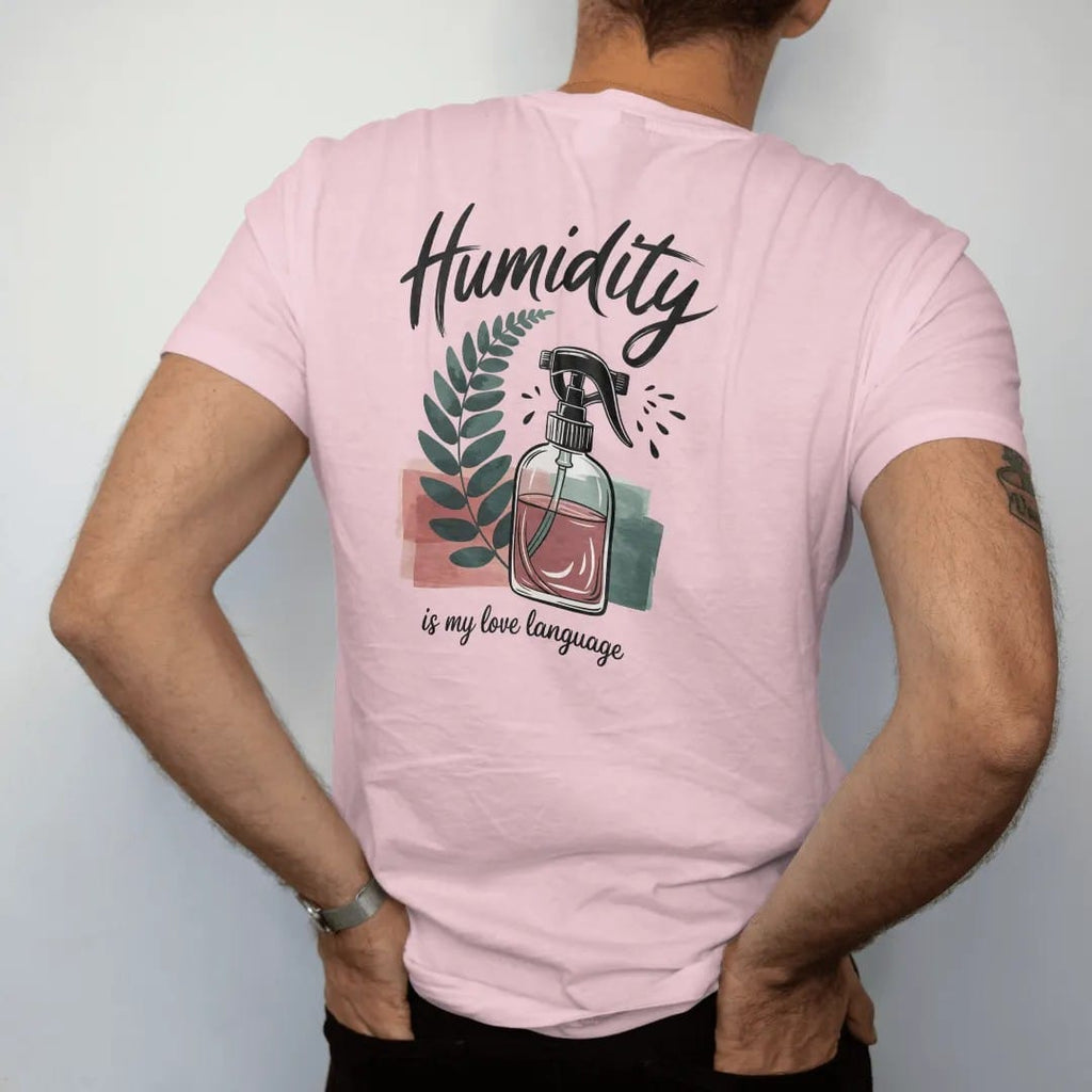 Man wearing a Blossom tee, seen from the back: a small fern beside a fine-mist spray bottle with tiny droplets, "HUMIDITY" in loose brush script above and "IS MY LOVE LANGUAGE" small below, painted in loose watercolor and ink with soft deep green,…