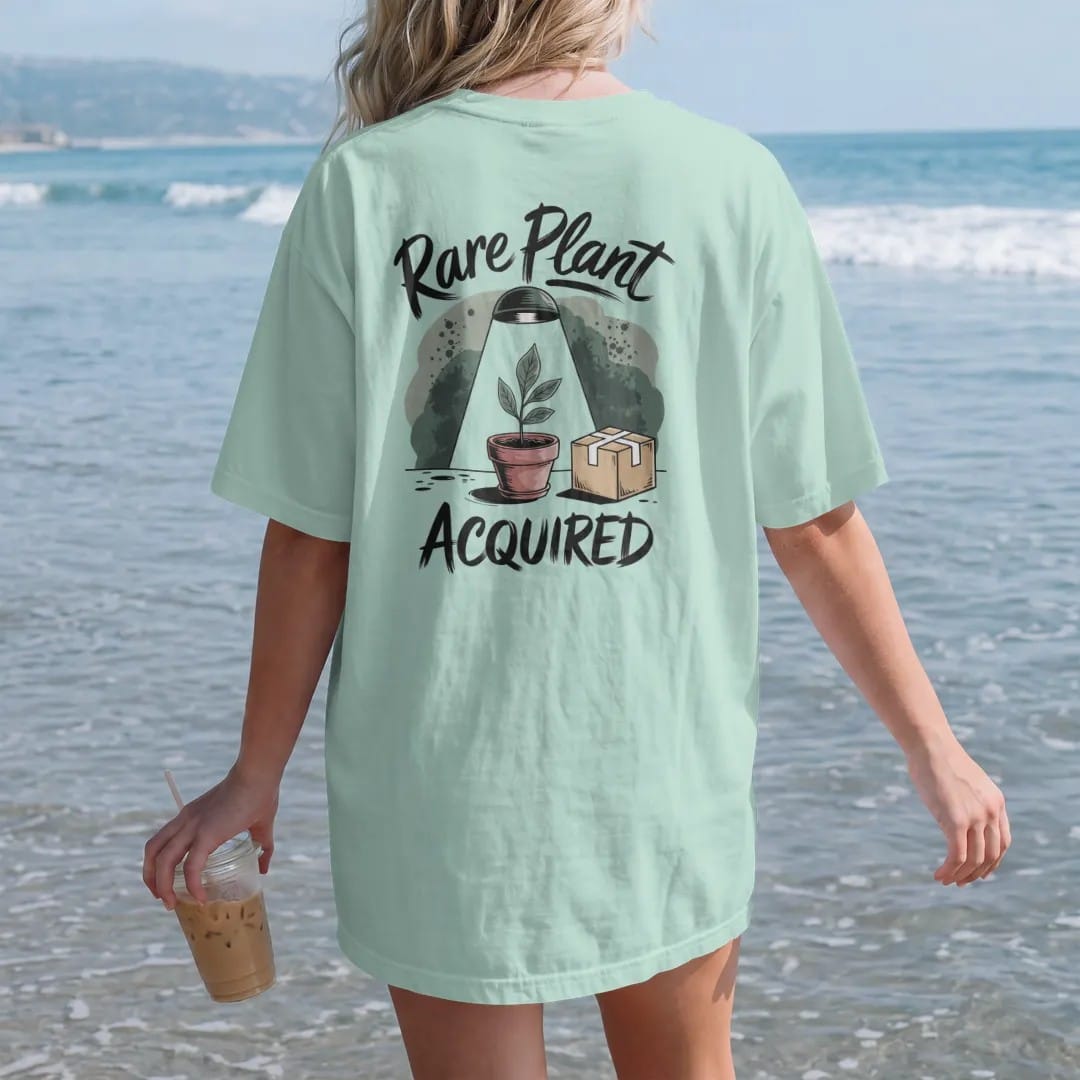 Woman on the beach in a Chalky Mint tee, back view: a single small pot with one prized leaf under a tiny spotlight, a little cardboard shipping box beside it, "RARE PLANT" in loose brush script above and "ACQUIRED" below, painted in loose…