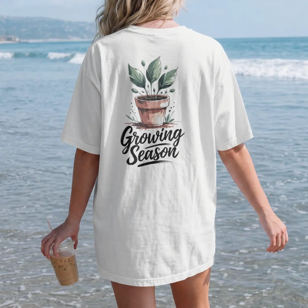 Woman on the beach in a White tee, back view: a small pot sprouting three fresh leaves with a few tiny buds, "GROWING SEASON" in hand-lettered brush script beneath, painted in loose watercolor and ink with soft deep green, terracotta, soil brown…