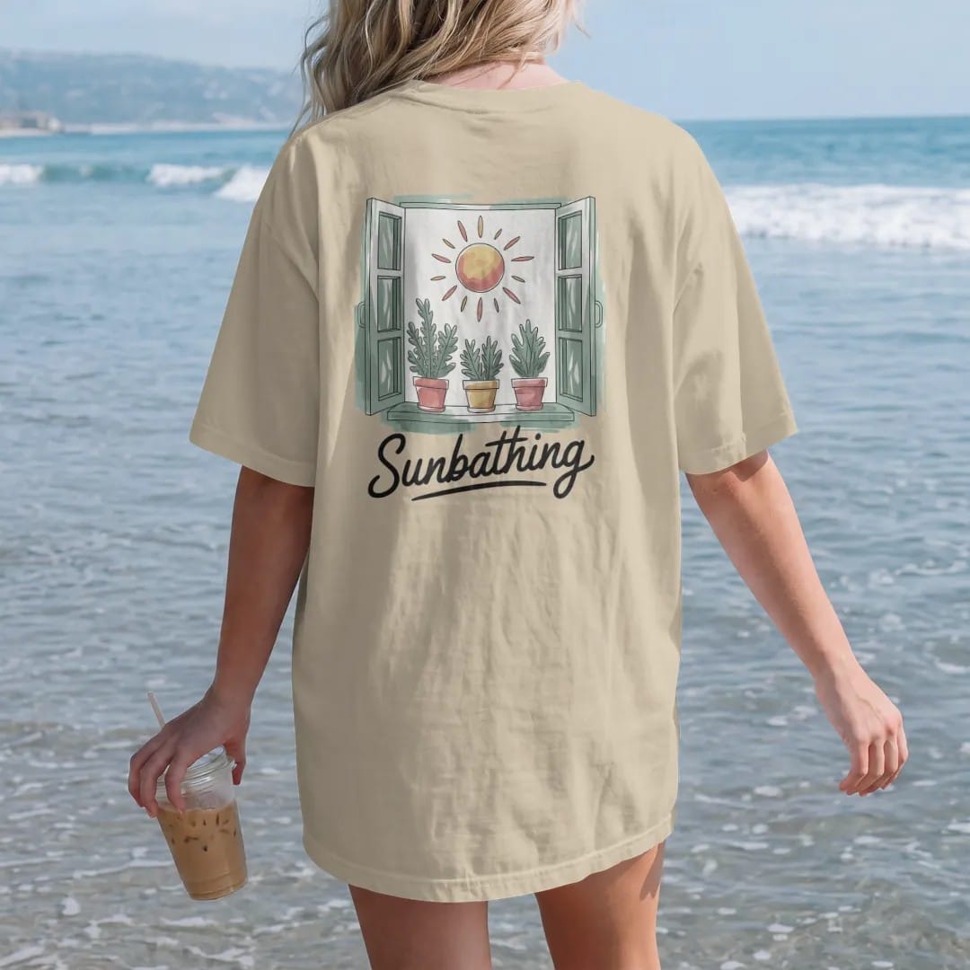 Woman on the beach in a Sandstone tee, back view: a sunny windowsill with three small potted plants leaning toward a round sun, "SUNBATHING" in loose brush script beneath, painted in loose watercolor and ink with soft deep green, terracotta, soil…