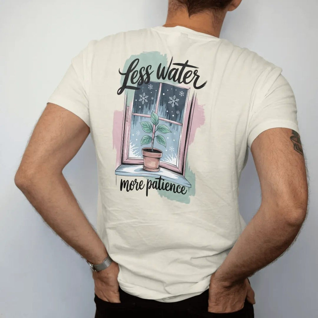Man wearing a Ivory tee, seen from the back: a small plant on a frosty windowsill with a few snowflakes outside the glass, "LESS WATER" in loose brush script above and "MORE PATIENCE" small below, painted in loose watercolor and ink with soft mint,…
