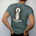 Man wearing a Blue Spruce tee, seen from the back: back print: A corked glass bottle of water under a full moon, rosemary sprigs around it, arched header "MOON WATER" above, small banner "STEEPED AT MIDNIGHT" below, detailed vintage etching, fine…
