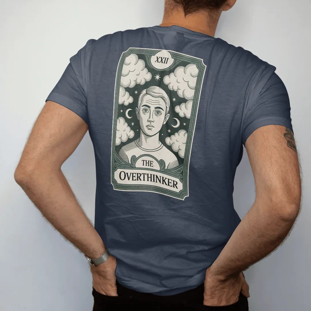 Man wearing a Midnight tee, seen from the back: back print: A tarot card frame with a wide-eyed figure surrounded by swirling thought clouds and tiny moons, Roman numeral "XXII" at the top, nameplate "THE OVERTHINKER" at the bottom, antique…
