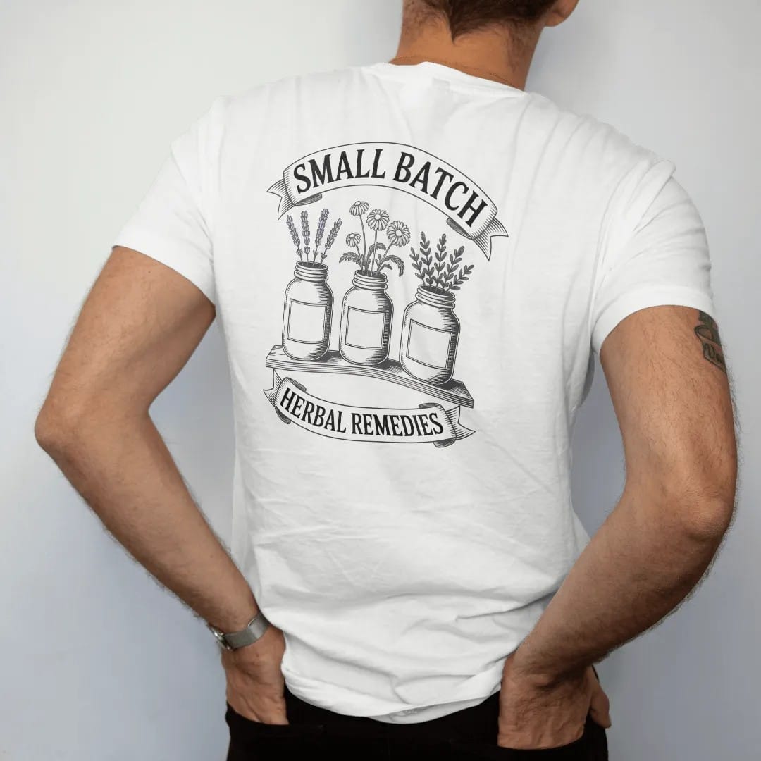 Man wearing a White tee, seen from the back: back print: three apothecary jars with blank labels holding lavender, chamomile and mugwort on a wooden shelf, curved header "SMALL BATCH" above, ribbon "HERBAL REMEDIES" below, detailed vintage etching,…