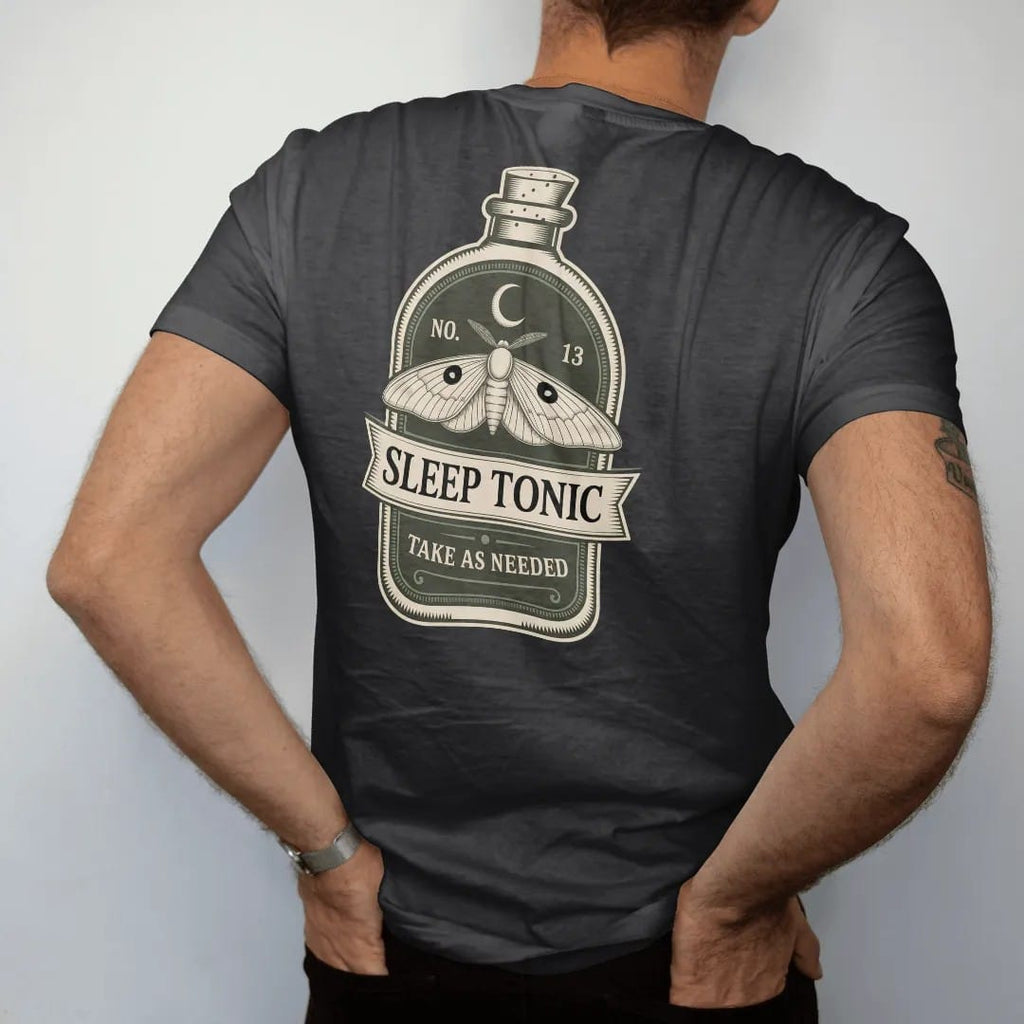 Man wearing a Black tee, seen from the back: back print: A vintage potion bottle label with a sleeping moth and a crescent moon, label layout with "NO. 13" on top, "SLEEP TONIC" in the center banner and "TAKE AS NEEDED" below, detailed vintage…