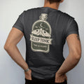 Man wearing a Black tee, seen from the back: back print: A vintage potion bottle label with a sleeping moth and a crescent moon, label layout with "NO. 13" on top, "SLEEP TONIC" in the center banner and "TAKE AS NEEDED" below, detailed vintage…