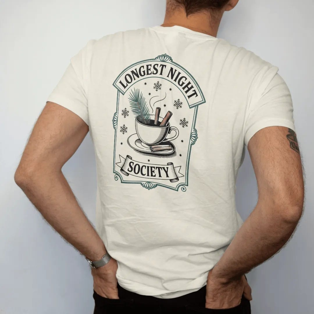Man wearing a Ivory tee, seen from the back: back print: A steaming teacup with a pine sprig and cinnamon sticks, surrounded by snowflakes and tiny stars, arched "LONGEST NIGHT" over the cup and "SOCIETY" in a small banner below, antique…