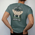 Man wearing a Blue Spruce tee, seen from the back: back print: A large luna moth with wings spread over two small potion bottles, arched "NIGHT SHIFT" above and "APOTHECARY" below, antique apothecary-label engraving, fine crosshatching, ornate…
