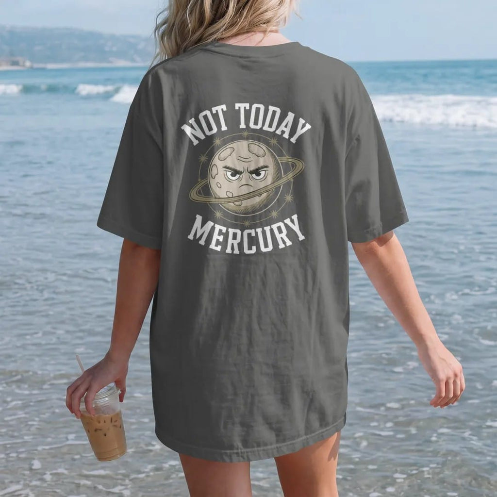 Woman on the beach in a Pepper tee, back view: back print: A tiny cratered planet with a grumpy face, circled by orbit lines and stars, stacked "NOT TODAY" above and "MERCURY" below, detailed vintage etching, fine crosshatching and stippling,…