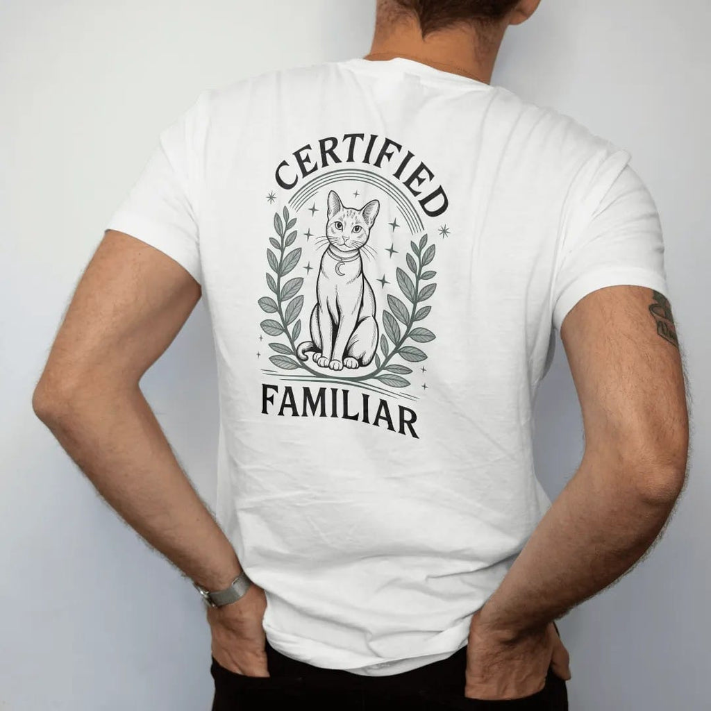 Man wearing a White tee, seen from the back: back print: A sleek cat drawn in light linework sitting upright with a crescent moon collar charm, framed by herbs and stars, arched "CERTIFIED" above and "FAMILIAR" below, detailed vintage etching, fine…