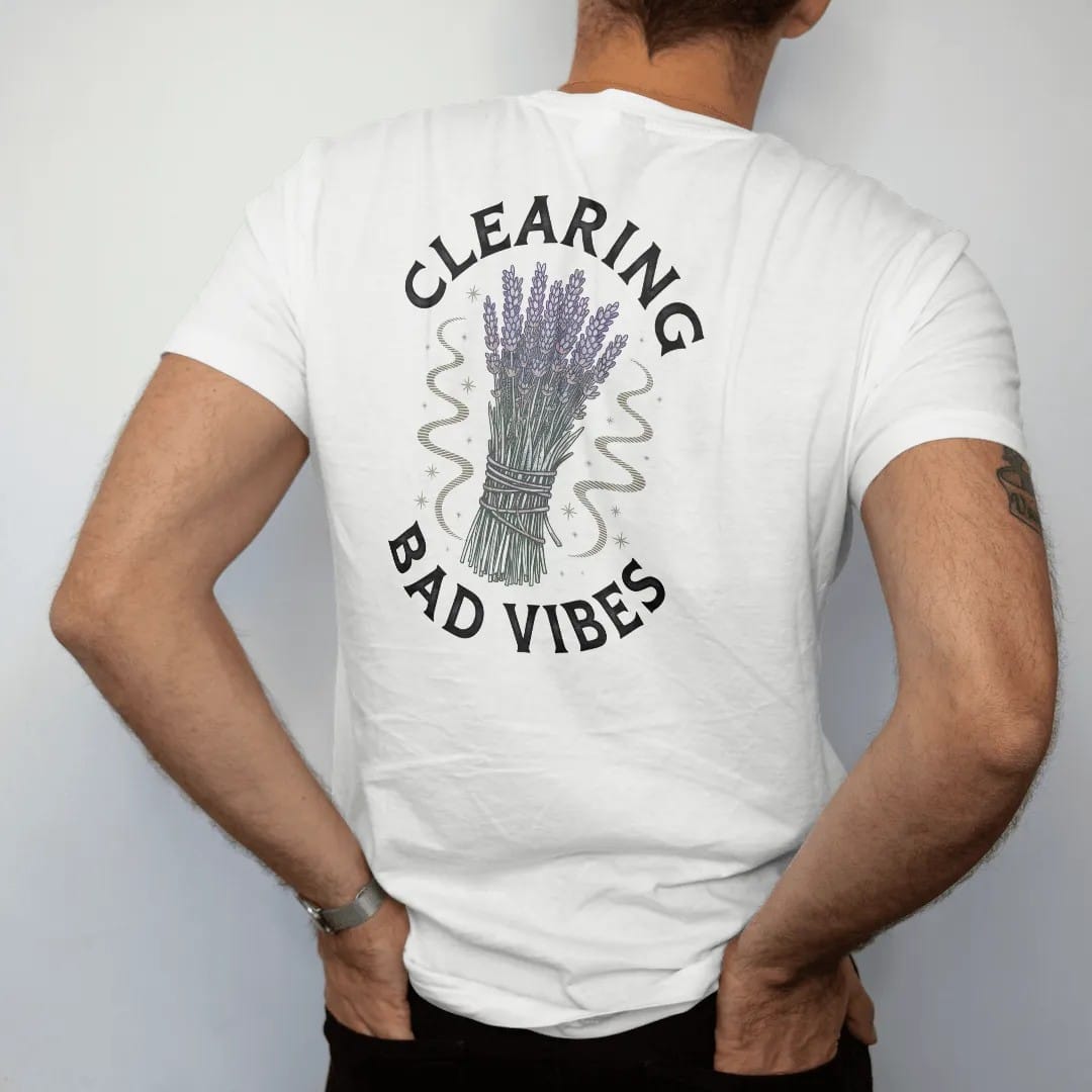 Man wearing a White tee, seen from the back: back print: A bundle of dried sage and lavender tied with string, its smoke curling into swirls and small stars, arched "CLEARING" above and "BAD VIBES" below, detailed vintage etching, fine…