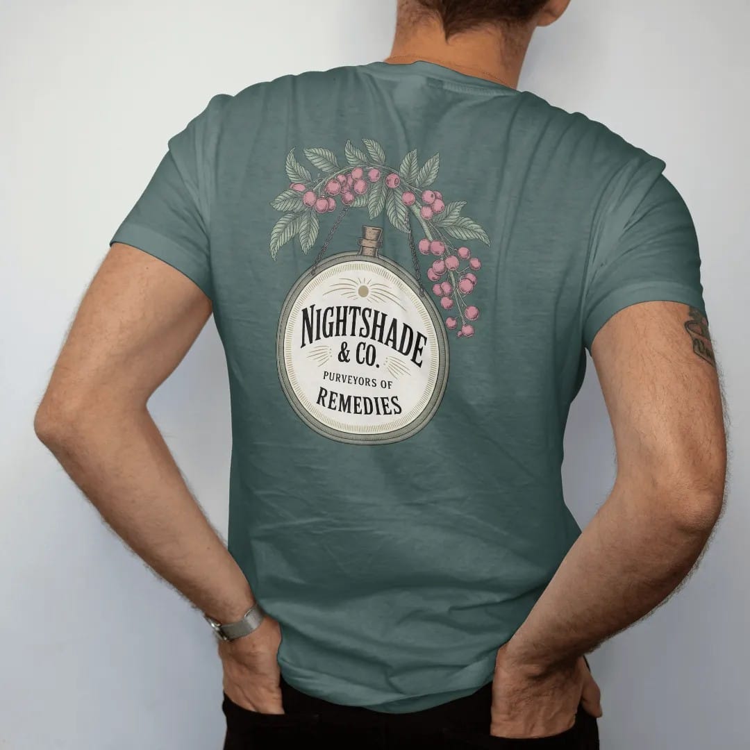 Man wearing a Blue Spruce tee, seen from the back: back print: A vintage hanging apothecary shop sign with a dangling bottle, framed by nightshade flowers and berries, hanging sign with "NIGHTSHADE & CO." large and "PURVEYORS OF REMEDIES" below,…