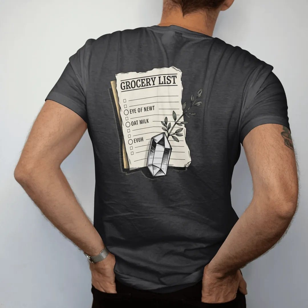 Man wearing a Black tee, seen from the back: back print: A torn vintage paper note held down by a small quartz crystal, with a sprig of thyme, list layout with header "GROCERY LIST" and the lines "EYE OF NEWT" and "OAT MILK", detailed vintage…
